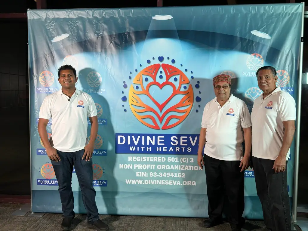 Three Divine Seva volunteers standing in front of the organization banner